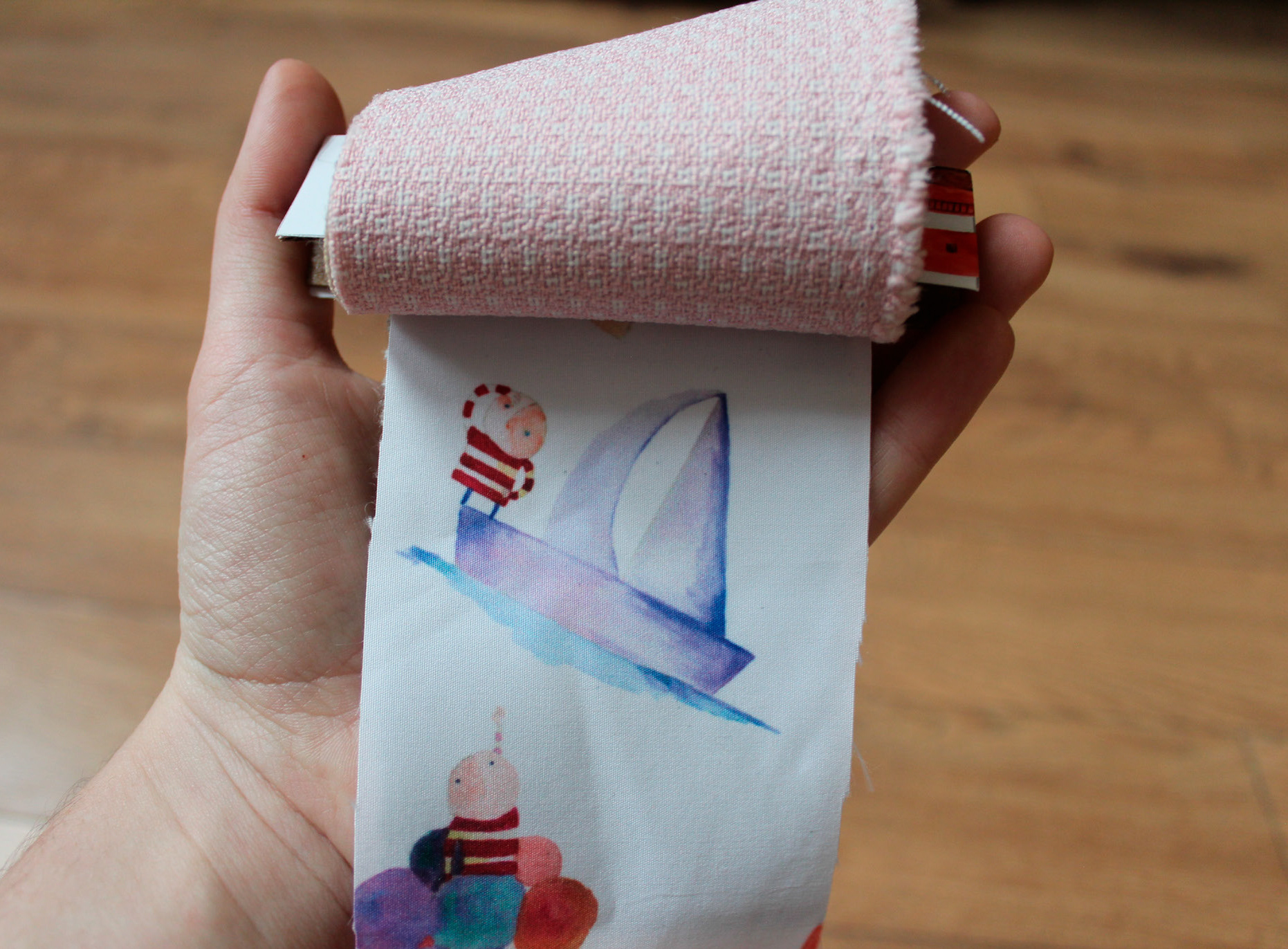 A hand holding a roll of printed fabric showing a Bellita sailboat illustration
